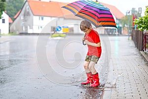 Kid boy wearing red rain boots and walking with umbrella