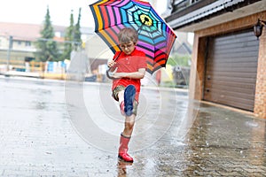 Kid boy wearing red rain boots and walking with umbrella