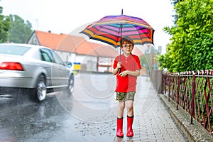 Kid boy wearing red rain boots and walking with umbrella