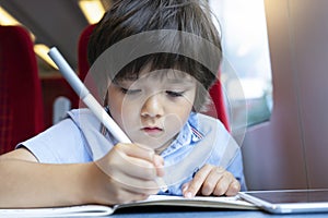 Kid boy wrinting on his book while traveling by the train, Child drawing or watching cartoon on teblet sitting by the window. Litt