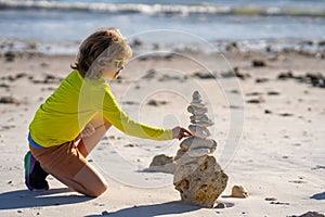 Kid boy with zen stones on sea beach, meditation, spa and harmony. Calm balance concept. Kids play on the beach. Calming