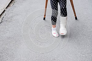 Kid with broken leg is on crutches on the street. conceptual photo depicting a child with a broken leg on a holiday, on