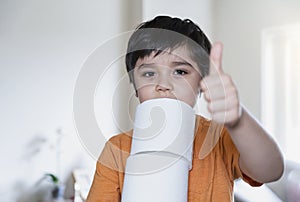 Kid carrying a stack of toilet paper with blurry living room background, Selective focus Child boy holding toilet roll showing