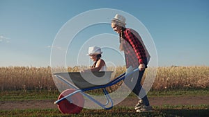 Kid children play with a garden trolley car ride on wheelbarrow. Happy family farming dream concept. Happy family