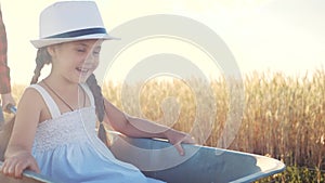 Kid children play with a garden trolley car ride on wheelbarrow. little girl child in hat happy family agriculture