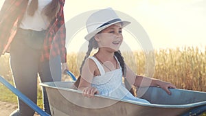 Kid children play with a garden trolley car ride on wheelbarrow. little girl child in hat happy family agriculture