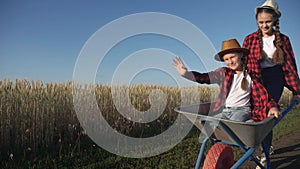 Kid children sisters play with a garden trolley car ride on wheelbarrow. Little girl child in hat happy family