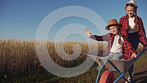 Kid children sisters play with a garden trolley car ride on wheelbarrow. Little girl child in hat happy family