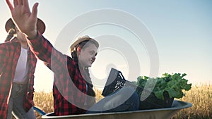 Kid children sisters play with a garden trolley car ride on wheelbarrow. Little girl child in hat happy family