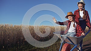 Kid children sisters play with a garden trolley car ride on wheelbarrow. little girl child in hat happy family