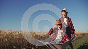 Kid children sisters play with a garden trolley car ride on wheelbarrow . little girl child in hat happy family