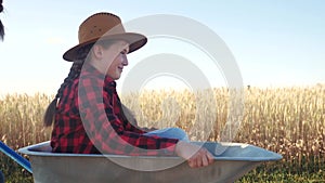 Kid children sisters play with a garden trolley car ride on wheelbarrow . little girl child in hat happy family