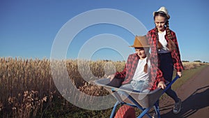 Kid children sisters play with a garden trolley car ride on wheelbarrow. little girl child in hat happy family