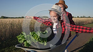 Kid children sisters play with a garden trolley car ride on wheelbarrow. little girl child in hat happy family