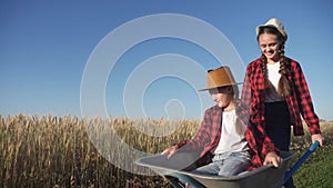 kid children sisters play with a garden trolley car ride on wheelbarrow . little girl child in hat happy family