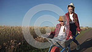 kid children sisters play with a garden trolley car ride on wheelbarrow. little girl child in hat happy family