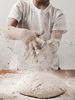 Kid clapping hands with flour over dough, vertical