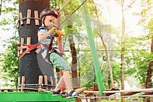 Kid climbing in high rope course in adventure park. Boy in safety helmet, extreme sport. Summer camp for kids