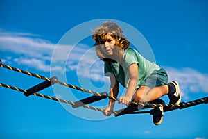 Kid climbing the net. Cute boy climbs up the ladder on the playground. Child climbs up the ladder against the blue sky.