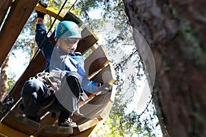 Kid climbing through wooden pipe in forest adventure park