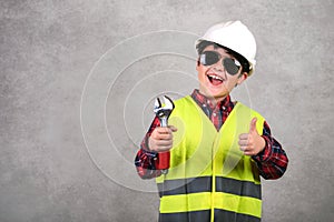 Kid construction worker in white helmet and sunglasses and holding a wrench