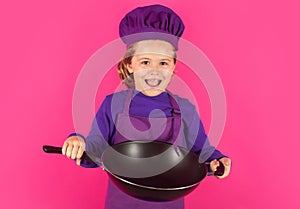 Kid cook with cooking pan. Excited chef cook. Child wearing cooker uniform and chef hat preparing food, studio portrait.