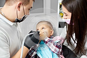 Kid in dental chair closes mouth with hands, fearing dentist