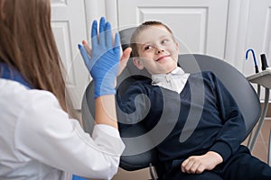 Kid in dental chair with dentist satisfied after repairing teeth giving five to doctor