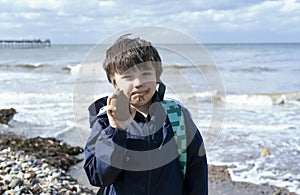 Kid with dirty mount of chocolate ice cream showing stone to the beach on spring or summer, Child boy playing with the rock,