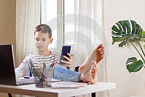 Kid distracting from online lesson or homework and playing video games, scrolling phone, texting on smartphone photo