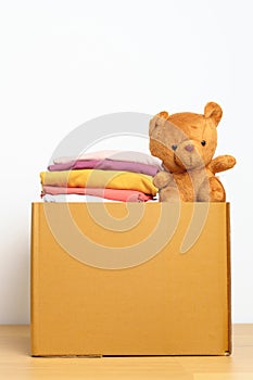 Kid Donation, Charity, Volunteer, Giving and Delivery Concept. Hand donate Bear doll and Clothes into cardboard box at home for