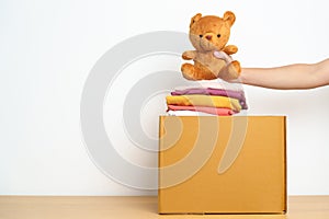 Kid Donation, Charity, Volunteer, Giving and Delivery Concept. Hand donate Bear doll and Clothes into cardboard box at home for