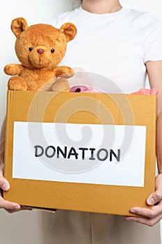 Kid Donation, Charity, Volunteer, Giving and Delivery Concept. Hand holding Bear doll and Clothes into Donation box at home for