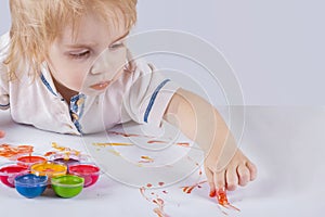 The kid draws with his fingers soiled with paint in paper