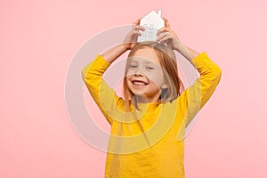 Kid dreaming of home. Happy charming cute little girl holding paper house on head and smiling to camera