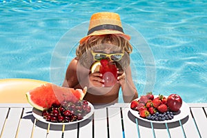Kid drink cocktail, strawberry smoothie in the pool. Child in swimming pool with summer fruits. Kids summer vacation