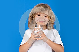 Kid drinking water, isolated on studio background. Portrait of happy smiling little child with glass of fresh water