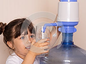 Kid drinks clean water from a transparent glass from manual drinking water pump at home.