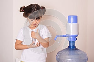 Kid drinks clean water from a transparent glass from manual drinking water pump at home.