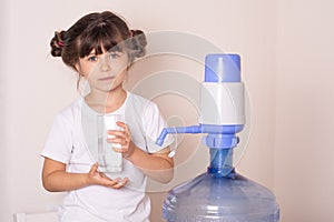 Kid drinks clean water from a transparent glass from manual drinking water pump at home.