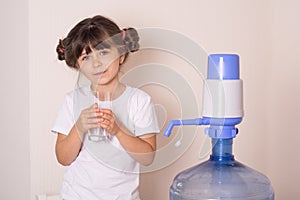 Kid drinks clean water from a transparent glass from manual drinking water pump at home.