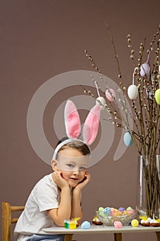 Kid dyeing Easter eggs. Child in bunny ears dye colorful egg for Easter hunt. Home decoration for spring holiday