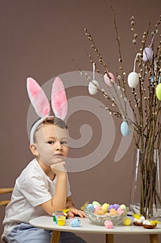 Kid dyeing Easter eggs. Children in bunny ears dye colorful egg for Easter hunt. Home decoration for spring holiday