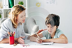 Kid with dyslexia drawing with pencil and child psychologist photo