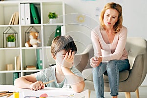 Kid with dyslexia holding pencil and child psychologist on background
