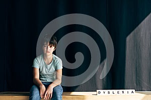 Kid with dyslexia looking at camera and sitting n with lettering dyslexia