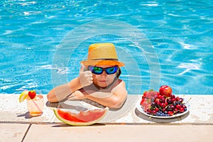 Kid eating fresh fruits on watter pool. Child in swimming pool playing in summer water. Vacation and traveling with kids