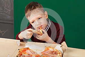 Kid eating pizza slice from the box at fast food restaurant.
