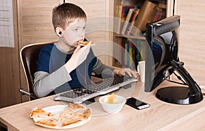 Kid eating pizza and surfing on internet or playing video games