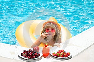 Kid eating summer fruits on watter pool. Child in swimming pool playing in summer water. Vacation and traveling with